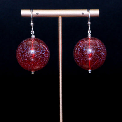 Red handblown glass earrings against a black background