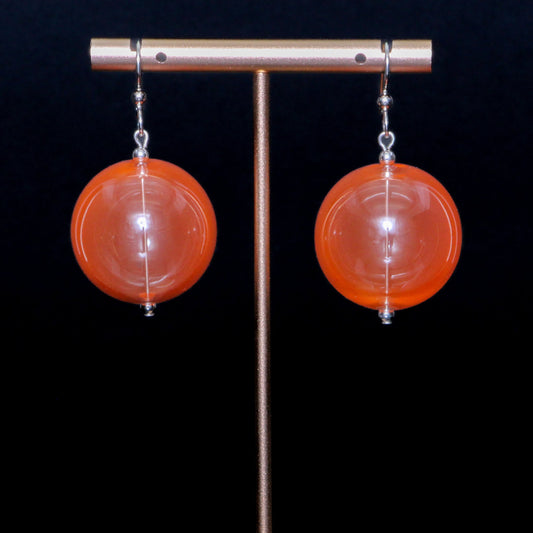 Coral orange handblown glass earrings against a black background