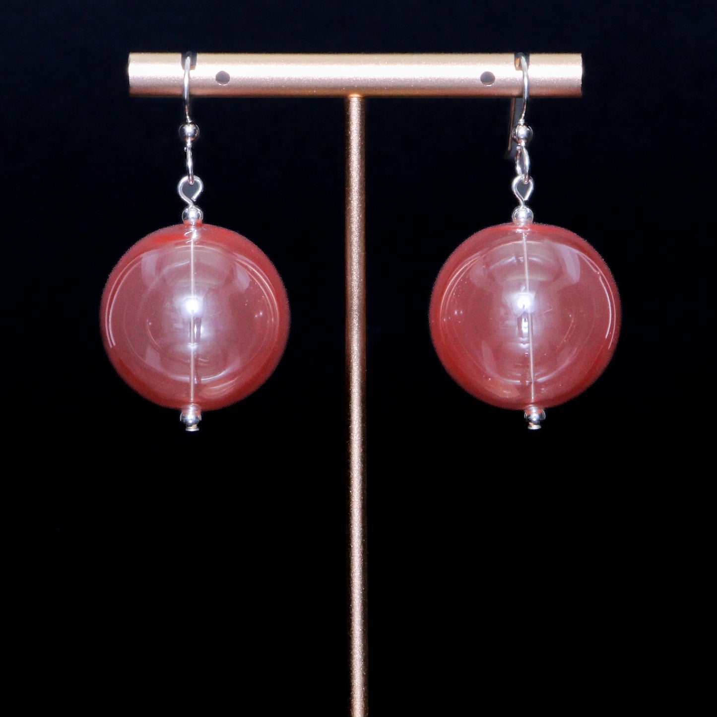 Coral red handblown glass earrings against a black background