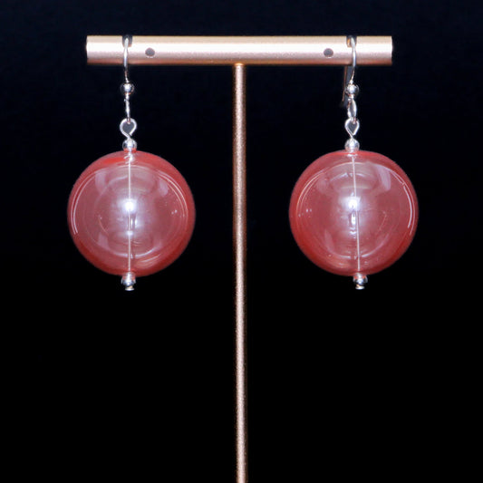 Coral red handblown glass earrings against a black background