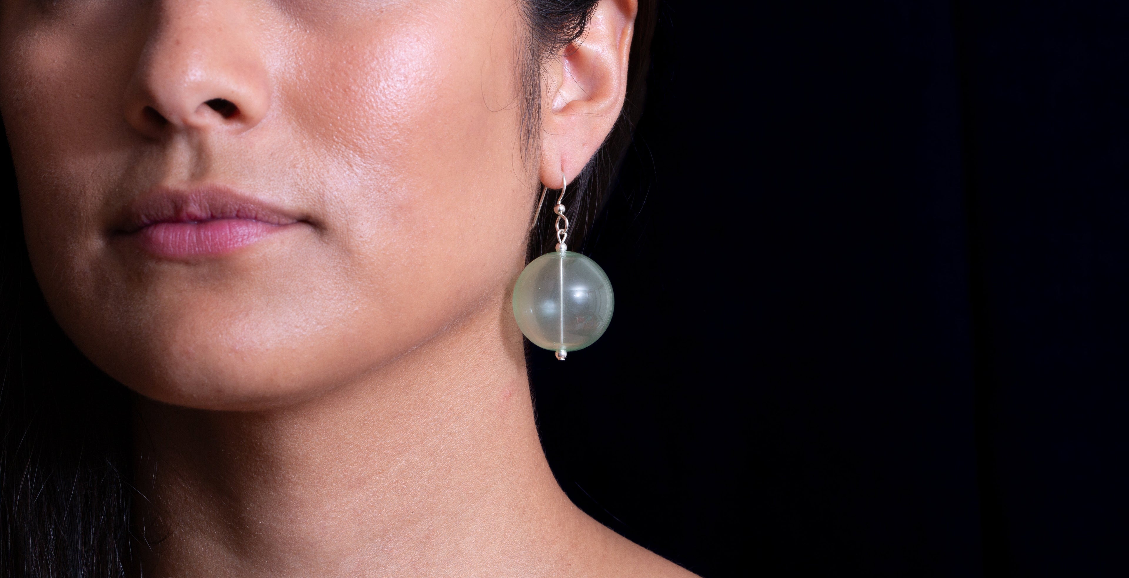 Woman wearing a glass earring against a black background